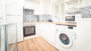 A compact kitchen with white cabinets, a washing machine, a microwave, and a tiled backsplash. - Apartment Sol "Ferrol". (Ferrol)