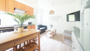 A modern kitchen with wooden cabinets, a dining table with chairs, a small side table, and a television mounted on the wall. - House O Carteiro "Cedeira". (Cedeira)