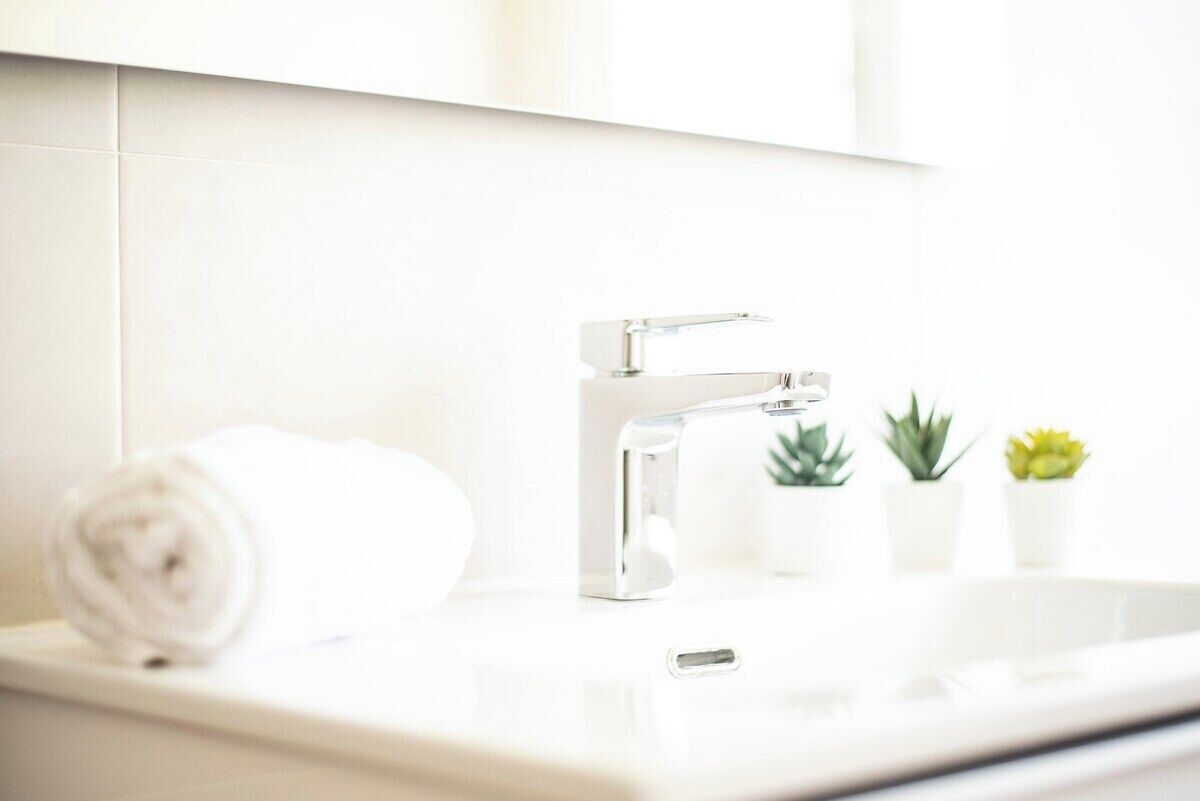 A bathroom with a white sink, a modern faucet, and a towel rolled up beside it.