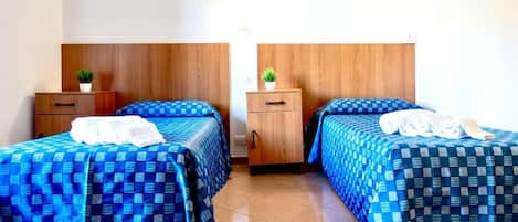 Habitación de hotel con dos camas, cada una con cubrecama azul a cuadros y toallas blancas. Poseen cabeceros de madera y una pequeña planta en cada mesita de noche.