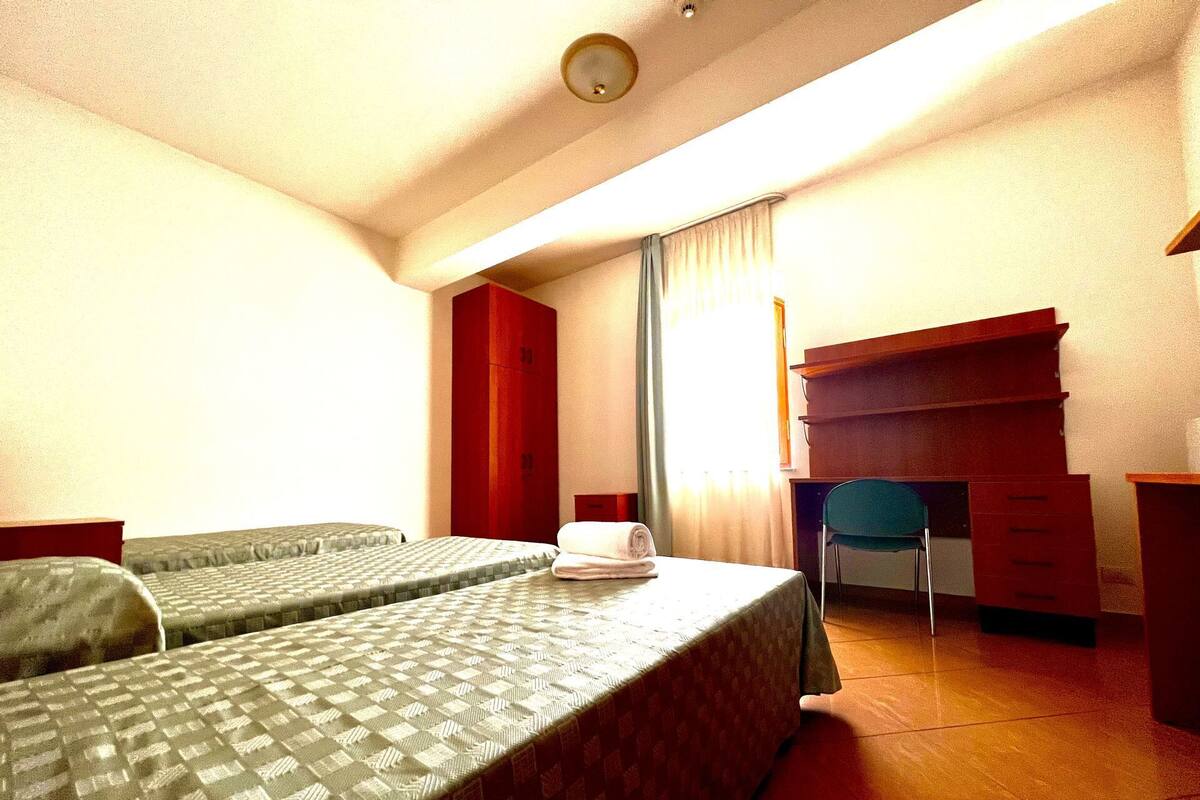 Una habitación de hotel con dos camas individuales, un escritorio, una silla y un armario.