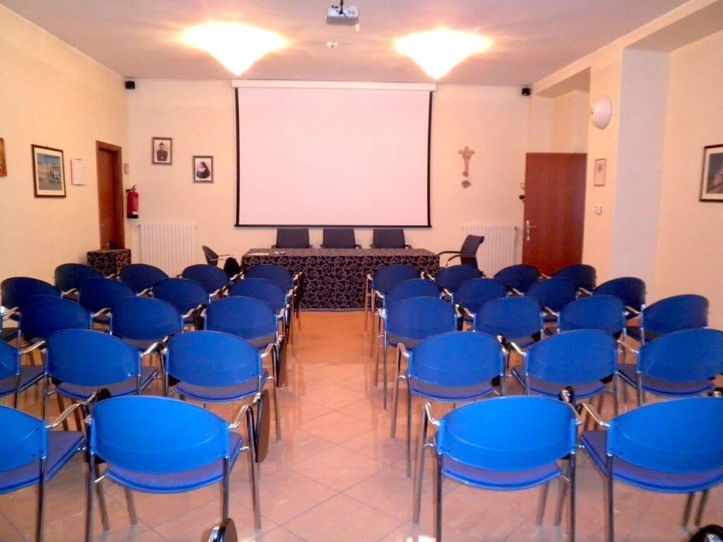 A conference room with rows of blue chairs, a projector screen, and a podium.