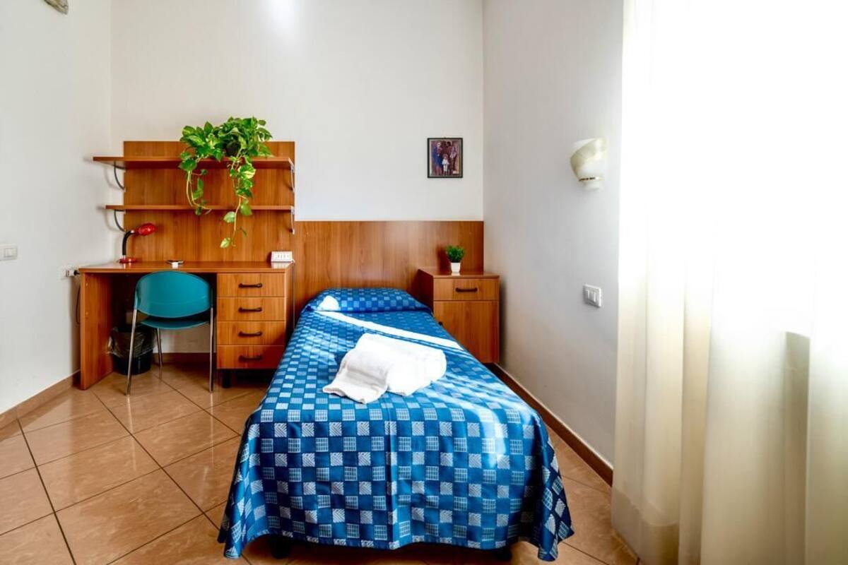 Un dormitorio con cama, escritorio, silla y estante con plantas.