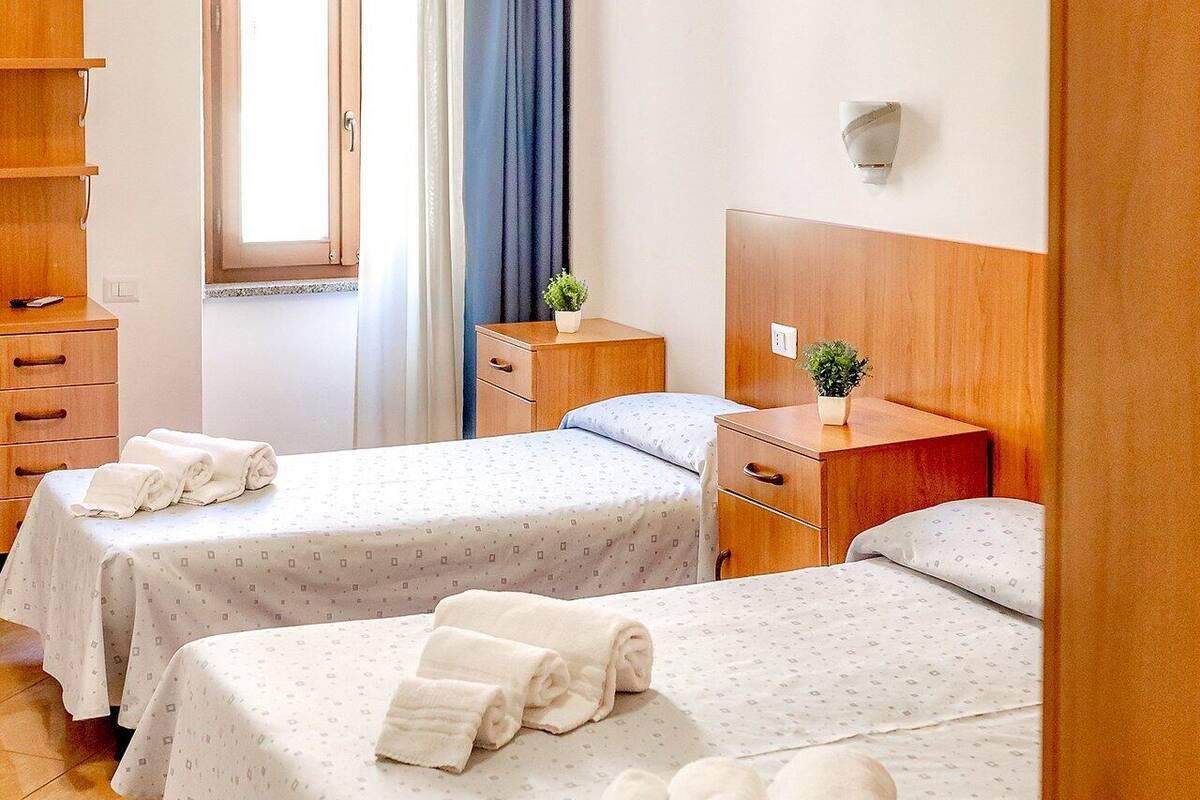 Habitación de hotel con dos camas, un aparador de madera, una mesita de noche, una ventana con cortinas y una planta pequeña.