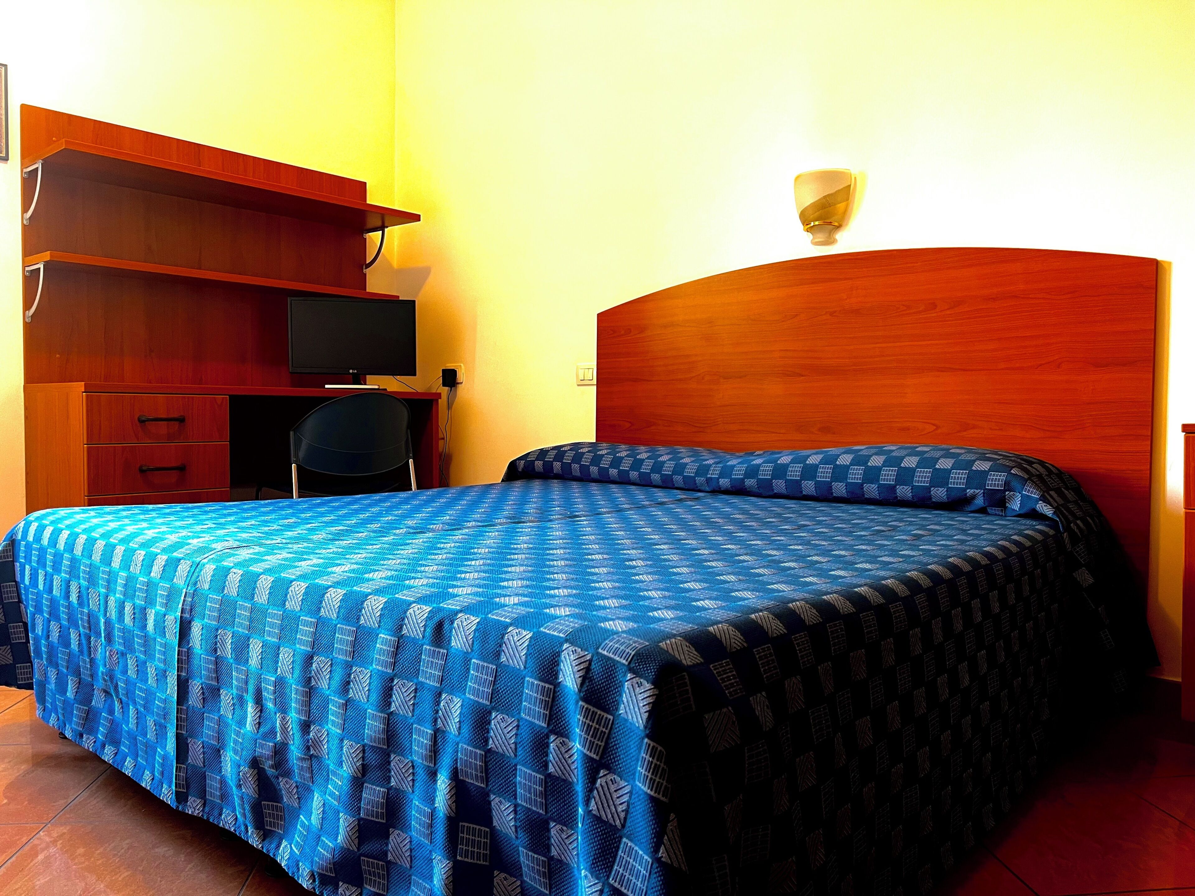 A bedroom with a bed, a desk, a chair, and a television.
