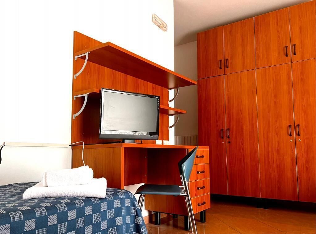 Ein Schlafzimmer mit einem Bett, einem Fernseher auf einem Holzregal, einem Sessel und einem Kleiderschrank.