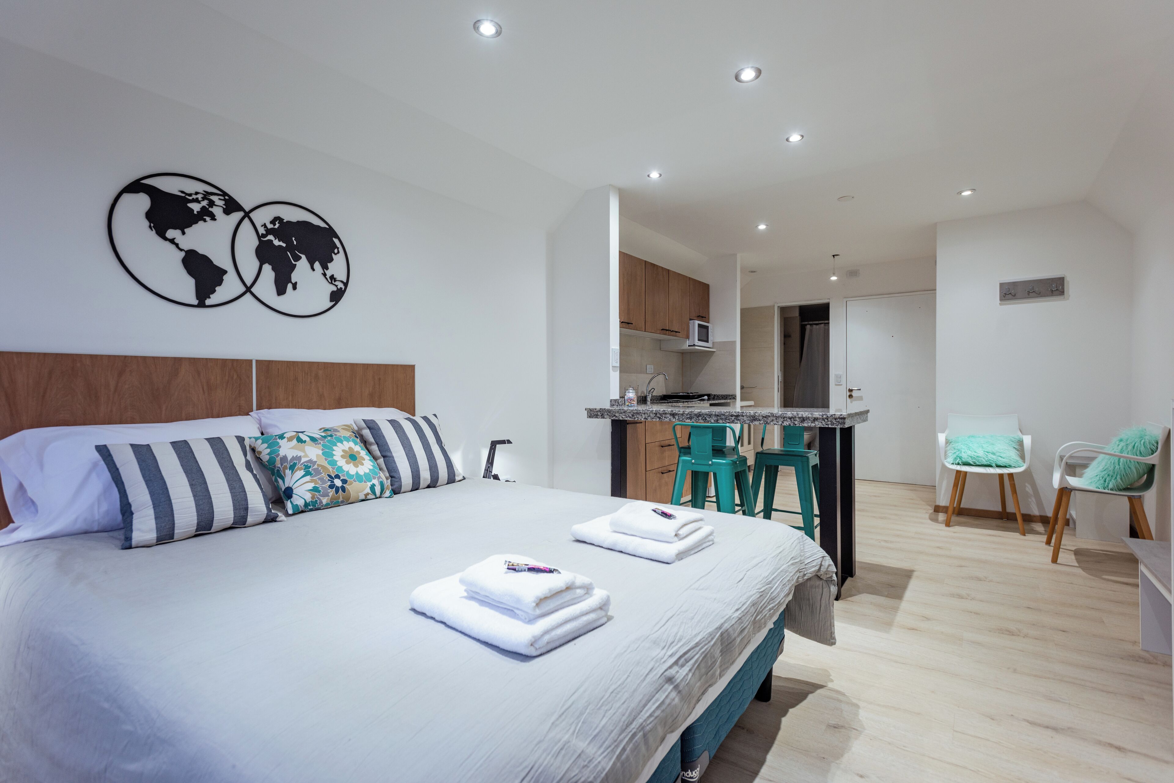 A modern hotel room with a large bed, a small kitchenette, and a dining area with two chairs.
