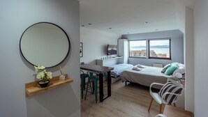 A modern bedroom with a bed, a desk, and a chair. There is a large window with a view of buildings and a cityscape. - Gente del Sur - Finisterre (Ushuaia)