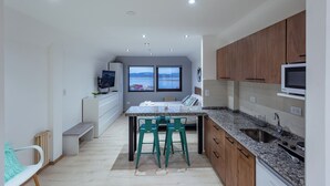 A modern kitchen with a granite countertop, wooden cabinets, and a built-in oven. There is a window with a view of the mountains, and a dining area with two green chairs. - Gente del Sur - Finisterre (Ushuaia)
