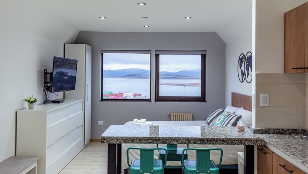 A compact kitchen with a dining area, two windows with a view, a TV, and a small plant. - Gente del Sur - Finisterre (Ushuaia)
