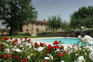 A stone building with a swimming pool surrounded by lush greenery and flowering plants. - Detached villa near Arezzo (Toscana)
