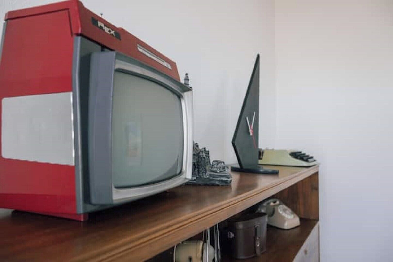 A television set on a wooden shelf with a small figurine and a clock.