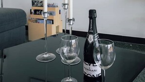 A room with a glass table displaying a bottle of Ferrari wine, three wine glasses, and two white candles. - [La terrazza di Chiavari] (Chiavari)