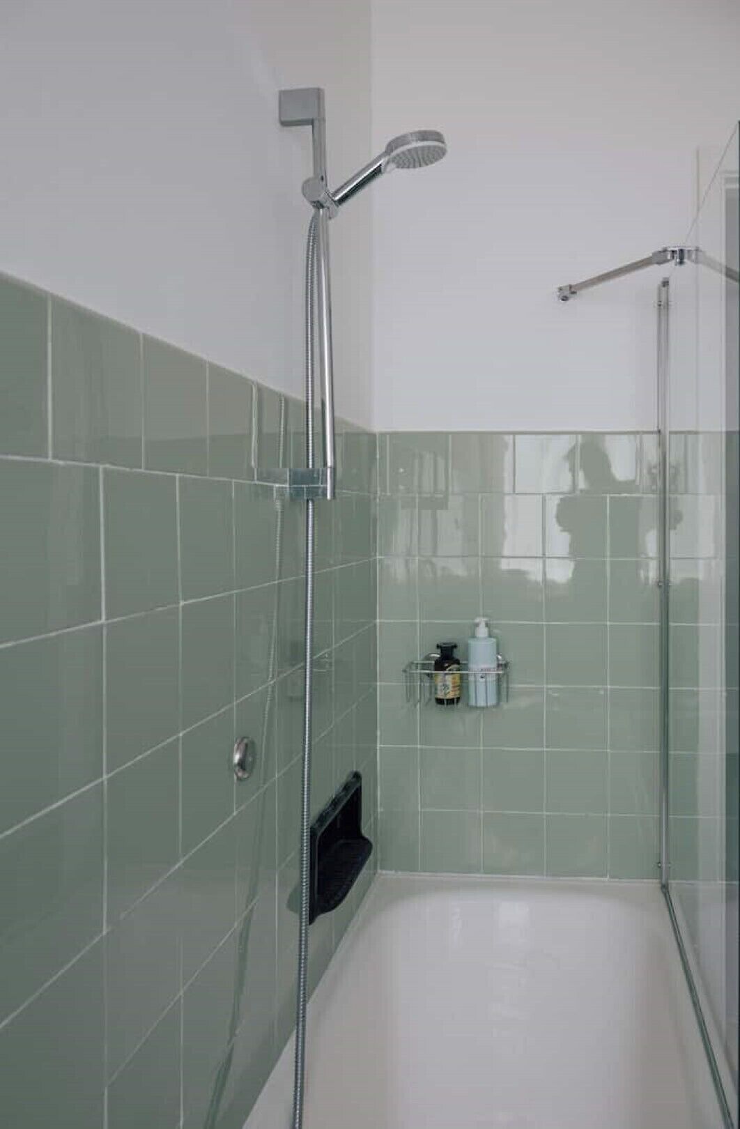 A modern bathroom with a glass-enclosed shower, a white bathtub, and a small shelf with toiletries.