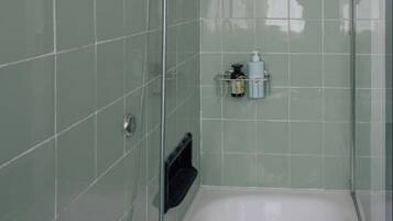 A modern bathroom with a glass-enclosed shower, a white bathtub, and a small shelf with toiletries.