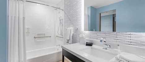 A modern bathroom with a bathtub, shower, and a large mirror.