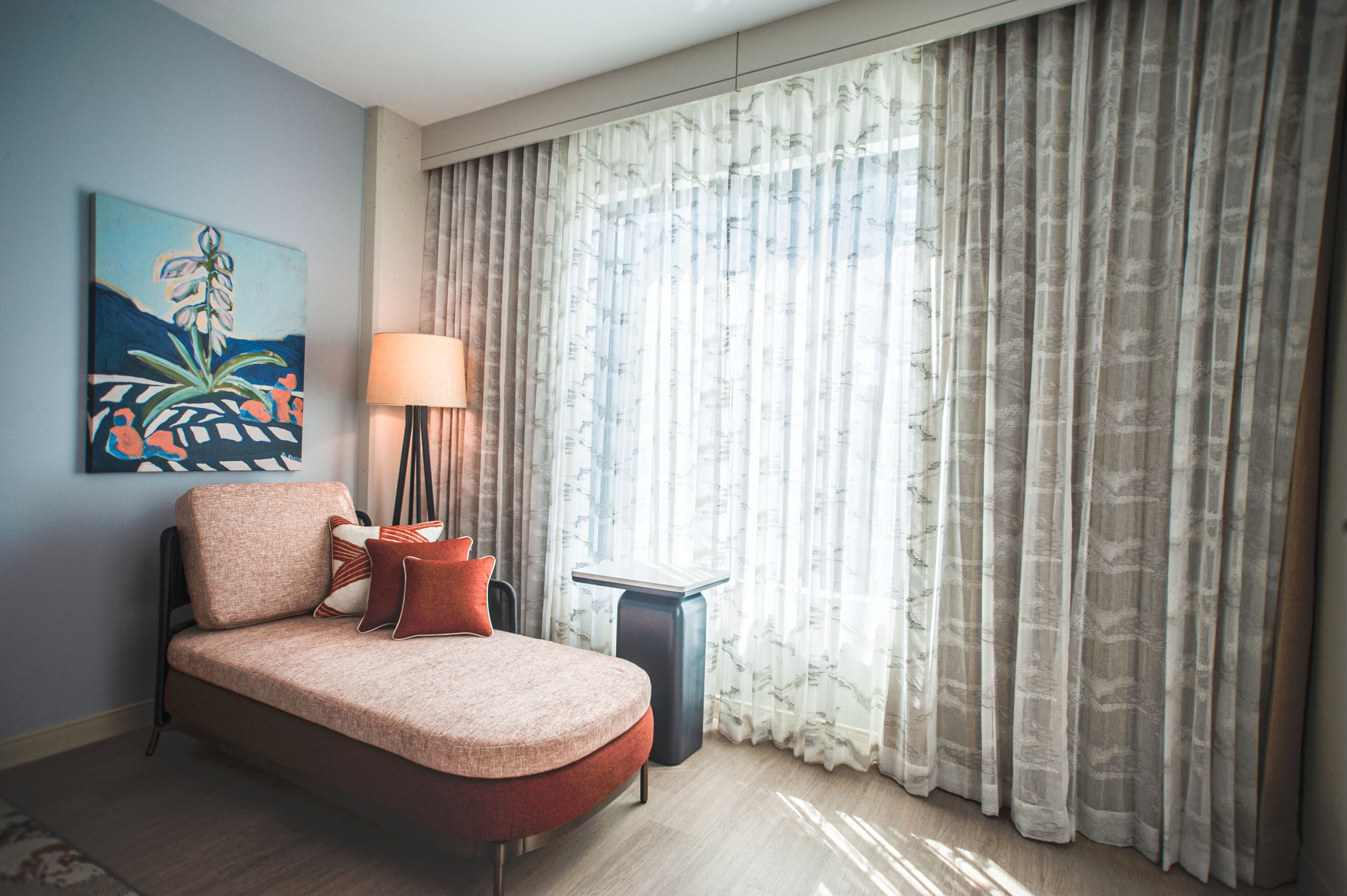 A modern bedroom with a sofa bed, a lamp, and a painting on the wall.