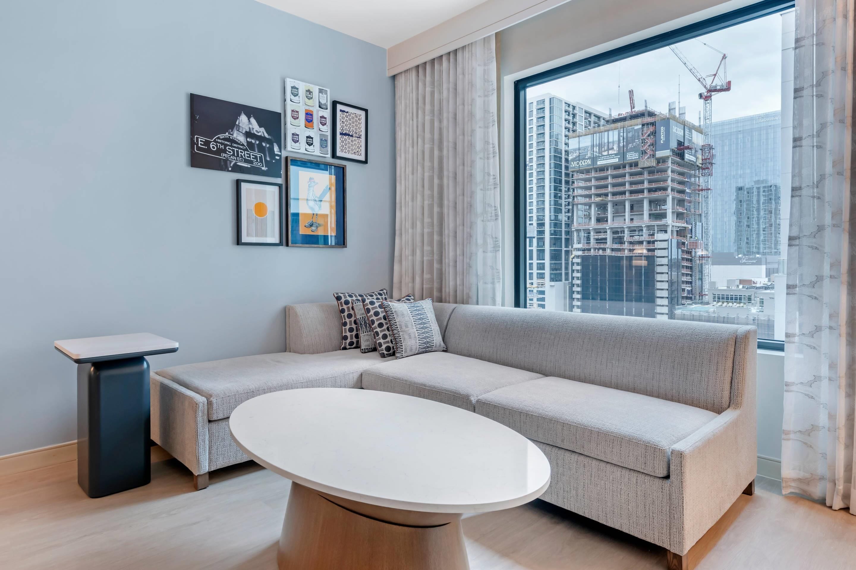 A modern living room with a sectional sofa, a round coffee table, and a large window with a city view.