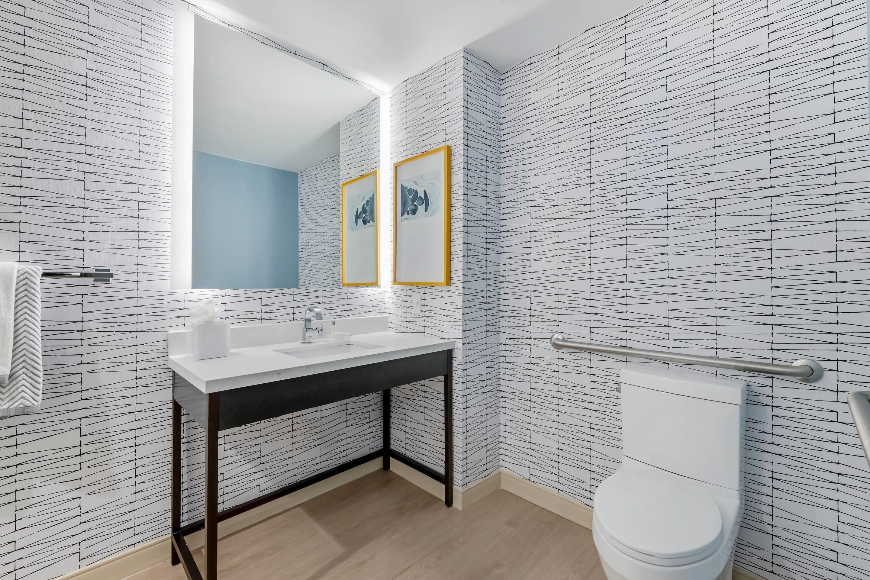 A modern bathroom with a white sink, mirror, and toilet, featuring a patterned wall and a blue accent wall.