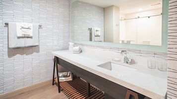 A modern bathroom with a white and black patterned wall, a large mirror, a white sink, and a wooden bench.