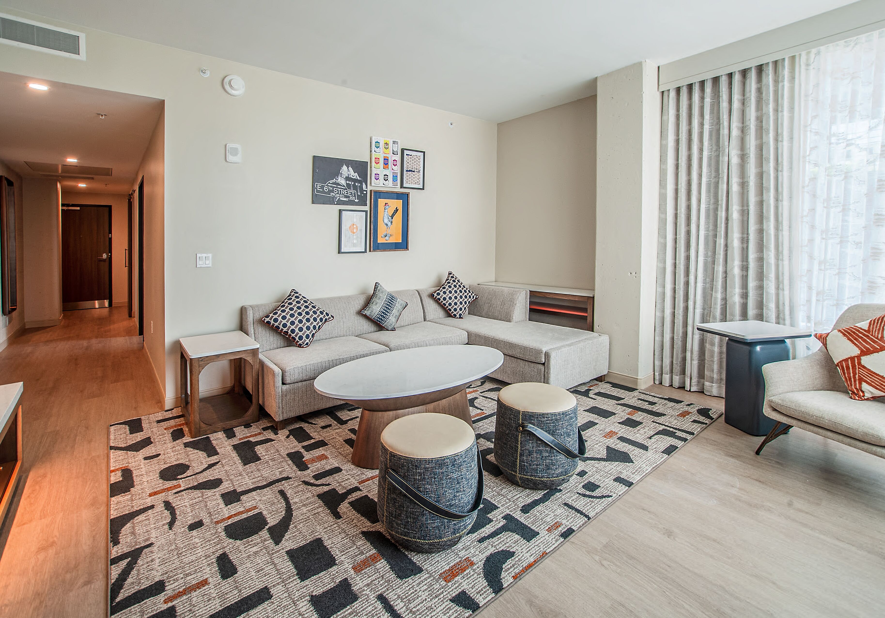 A modern living room with a sofa set, a coffee table, two ottomans, a patterned rug, and a side table.