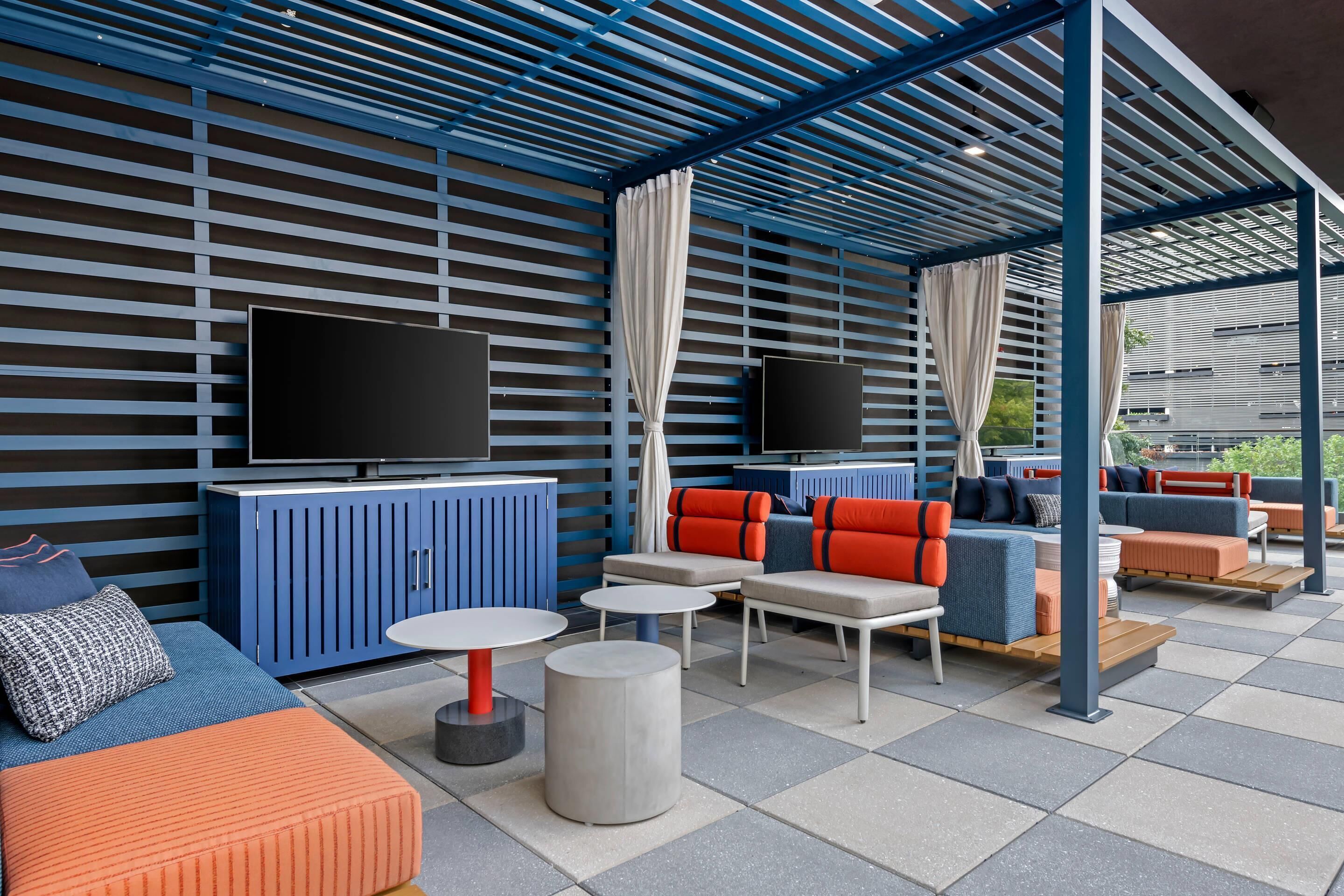 An outdoor seating area with blue and orange furniture, a flat-screen TV, and a covered section with a blue roof.