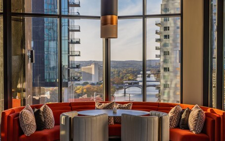 A modern interior with a red sofa, a round table, and a view of a cityscape through large windows.