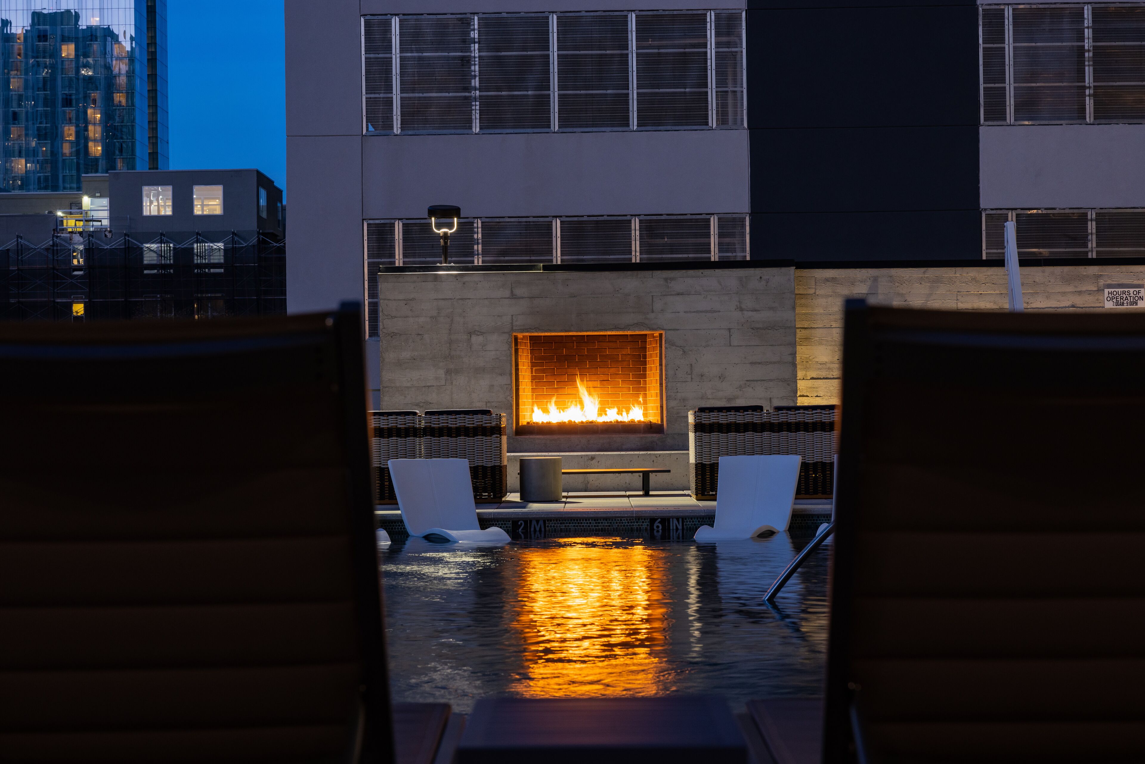 Zona de piscina con sillones de descanso, una chimenea y vistas al horizonte de la ciudad.