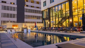 A hotel pool area with lounge chairs, a fire feature, and a large glass building in the background. - Cambria Hotel Austin Downtown (Austin)
