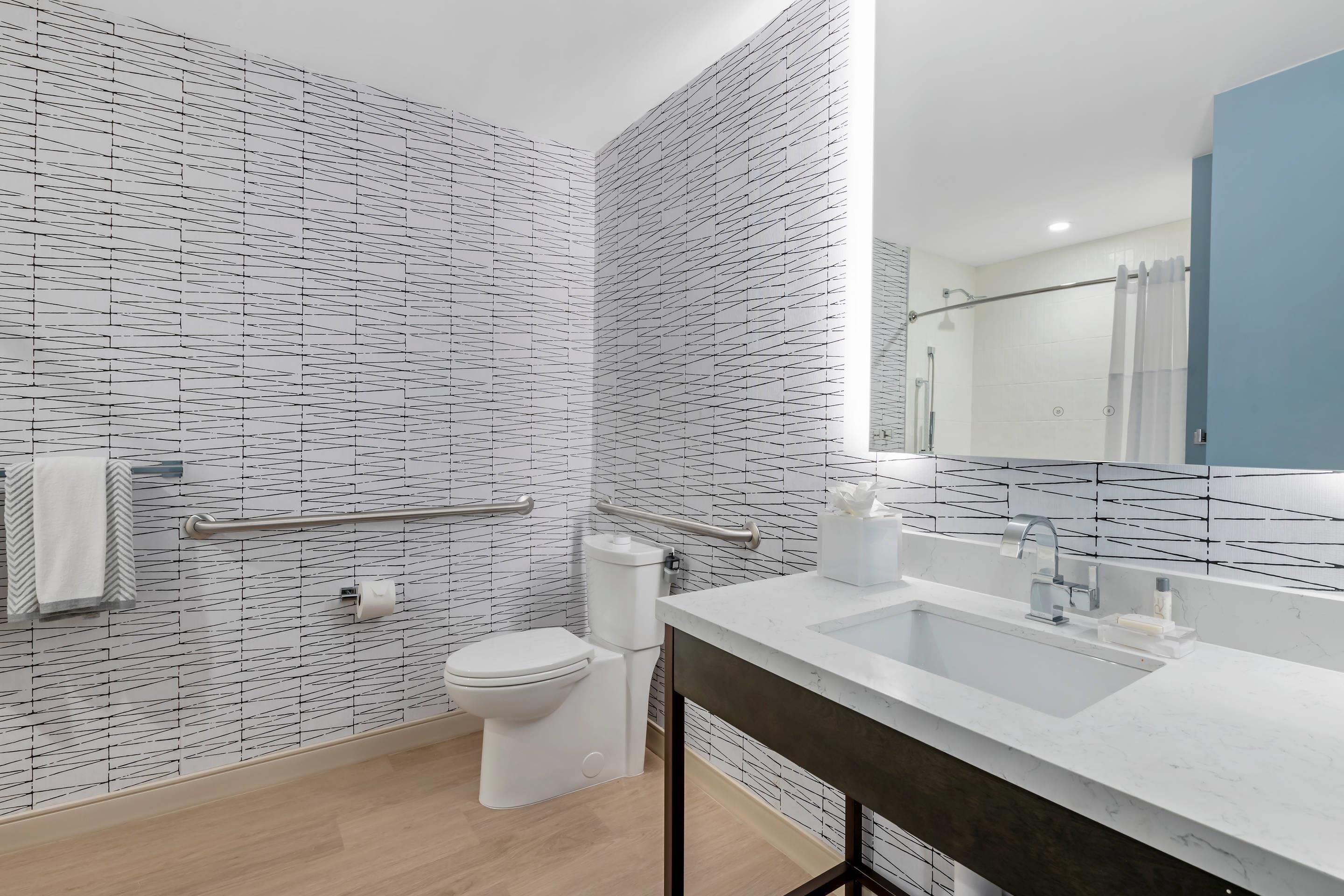 Un baño moderno con una pared de diseño en blanco y negro, un lavabo blanco con espejo y un inodoro.