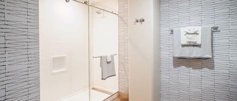 A modern bathroom with a glass shower enclosure, tiled walls, and a wooden floor.