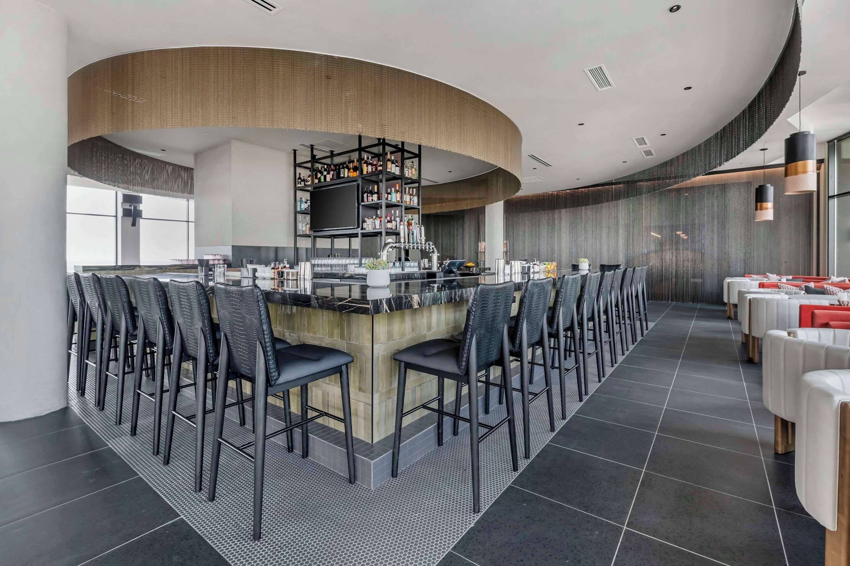 A modern bar area with a curved ceiling, black bar stools, and a central bar counter.
