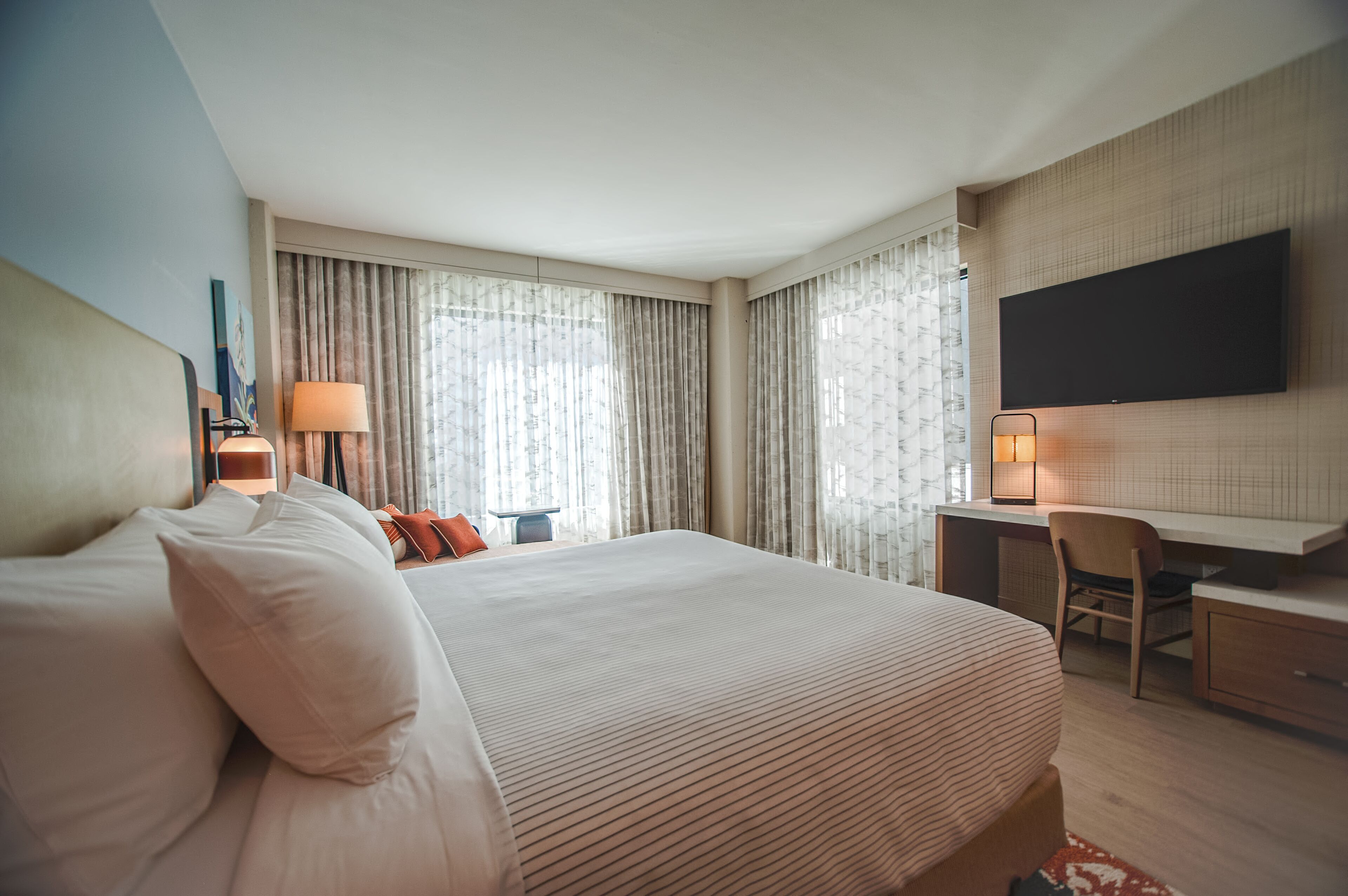 Une chambre d’hôtel avec un grand lit, un bureau, une chaise, un téléviseur à écran plat fixé au mur et une fenêtre avec des rideaux.