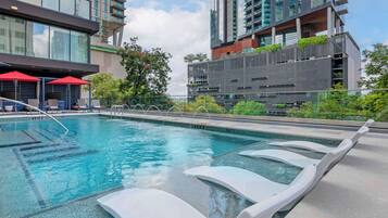 Relax by the pool surrounded by sleek lounge chairs and a glass barrier, offering a view of the surrounding high-rise buildings.