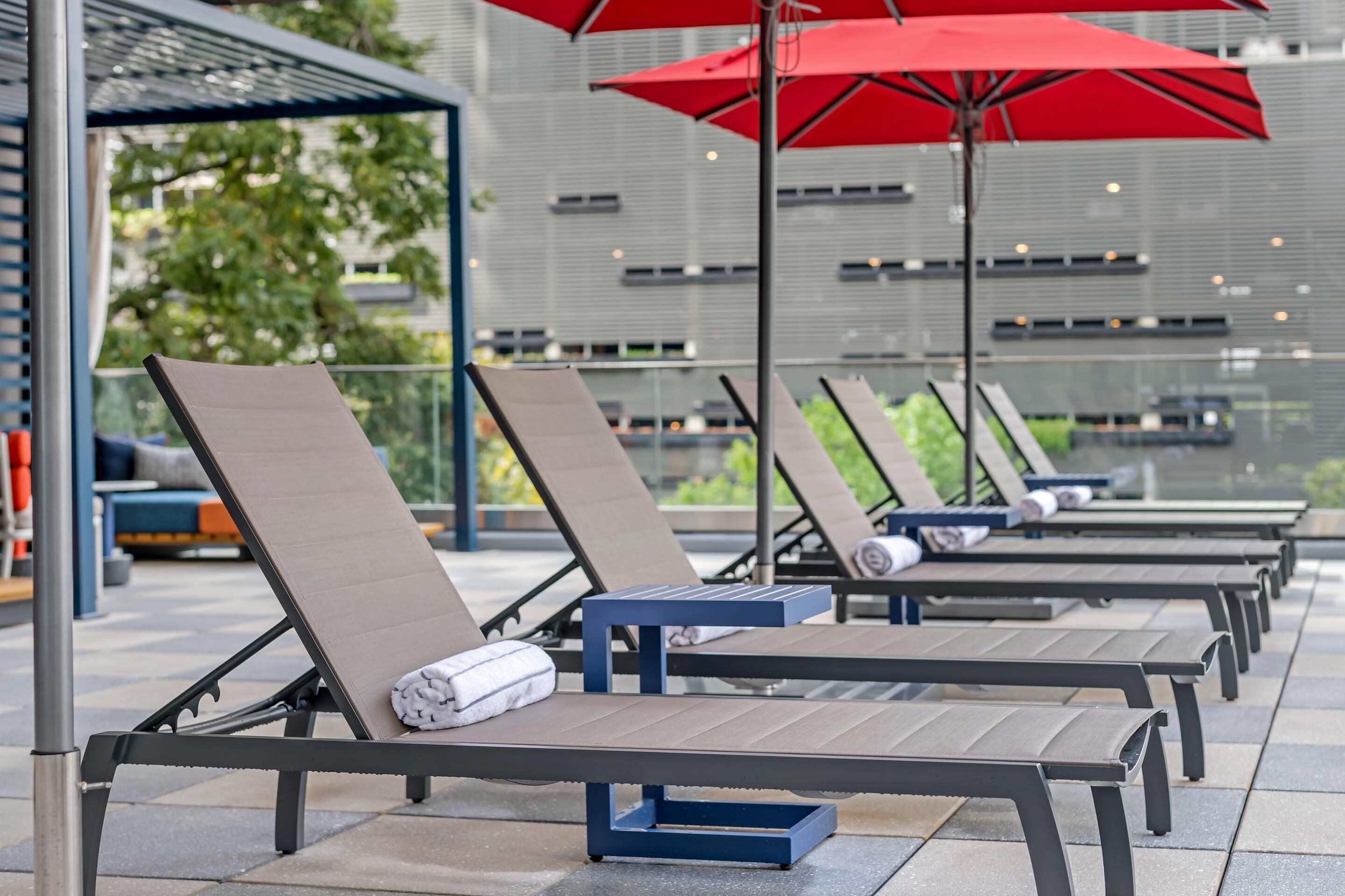 Outdoor lounge chairs with towels, a red umbrella, and a modern building in the background.