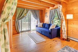 A cozy cabin interior with a blue sofa, wooden floors, and a large window with curtains. - Alexandria Cabin w/ Patio, Grill & Deck (Alexandria)