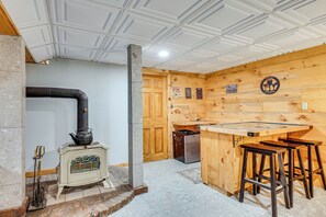 A kitchen with a wood-burning stove, wooden bar stools, and a refrigerator. - Alexandria Cabin w/ Patio, Grill & Deck (Alexandria)