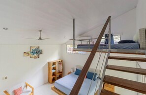 A dorm-style room with bunk beds, a ceiling fan, a wooden ladder, and a small wooden shelf unit.