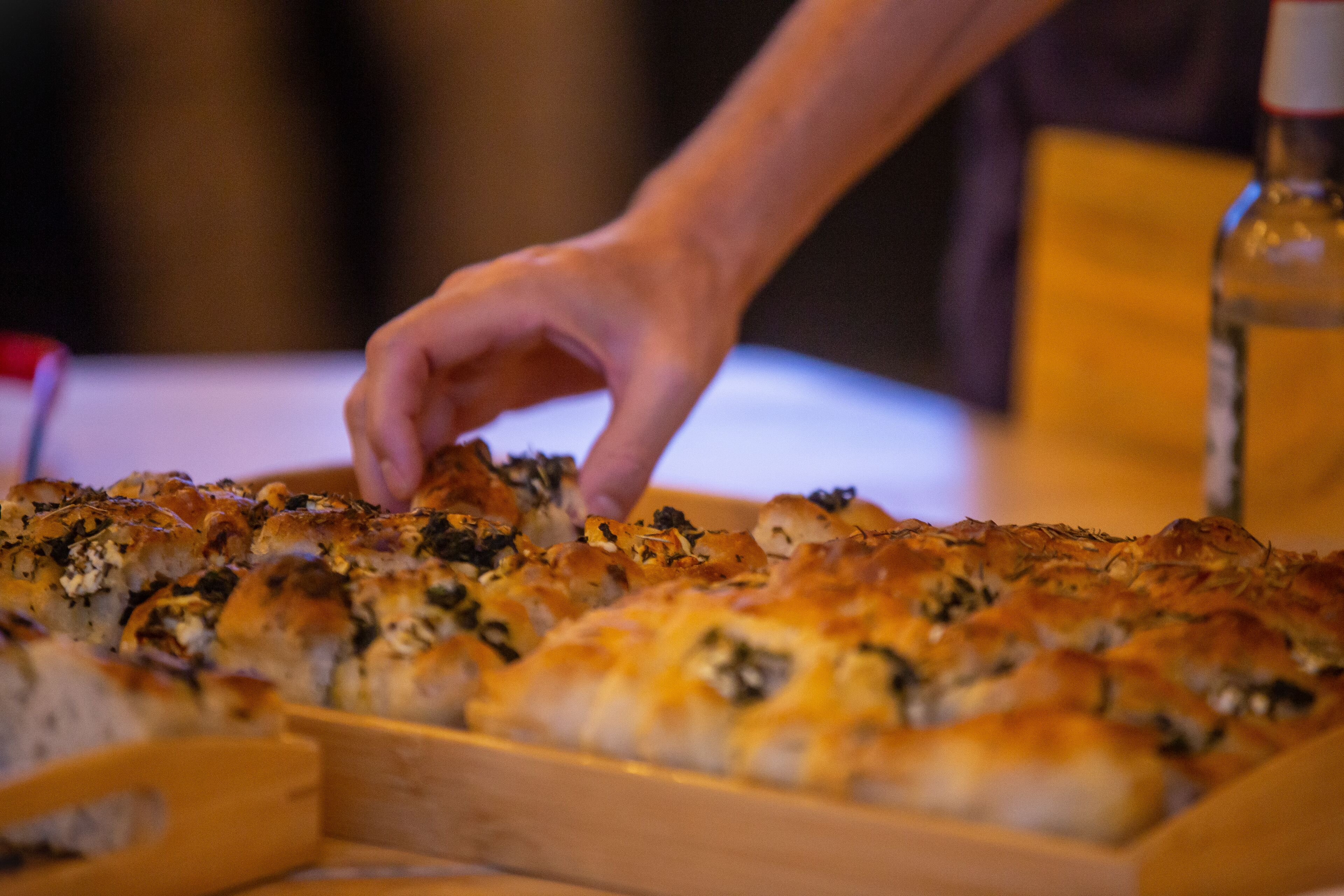 A tray of baked goods, possibly bread or pastries, with a hand reaching for one.
