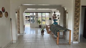 Un intérieur spacieux et bien éclairé, doté d’un sol carrelé, d’un coin repas avec une table et des chaises, et offrant une vue sur l’extérieur à travers une porte vitrée.