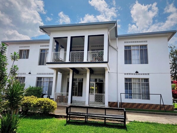 A two-story building with a balcony, a covered entrance, and a small garden area with a bench. - Tugende House (Kigali)