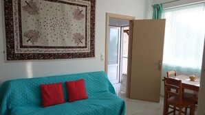 En tealgrøn sofa med to røde puder, et træspisebord med stole og et stort mønstret vægtæppe på væggen.