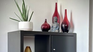 En svart hylla med en krukväxt, två röda vaser och en Buddha-staty.