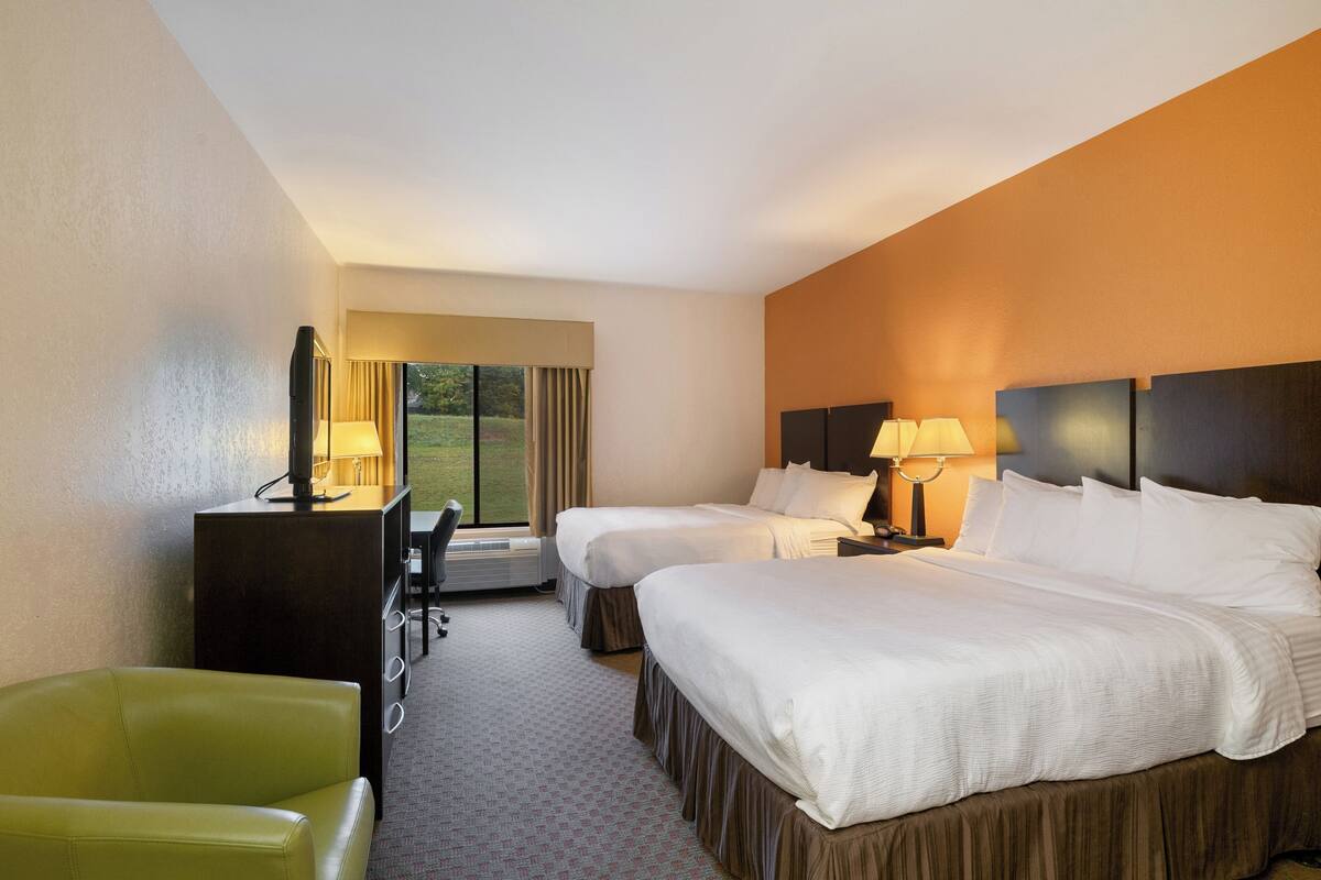 A hotel room with two beds, a desk, a chair, and a large window with curtains.