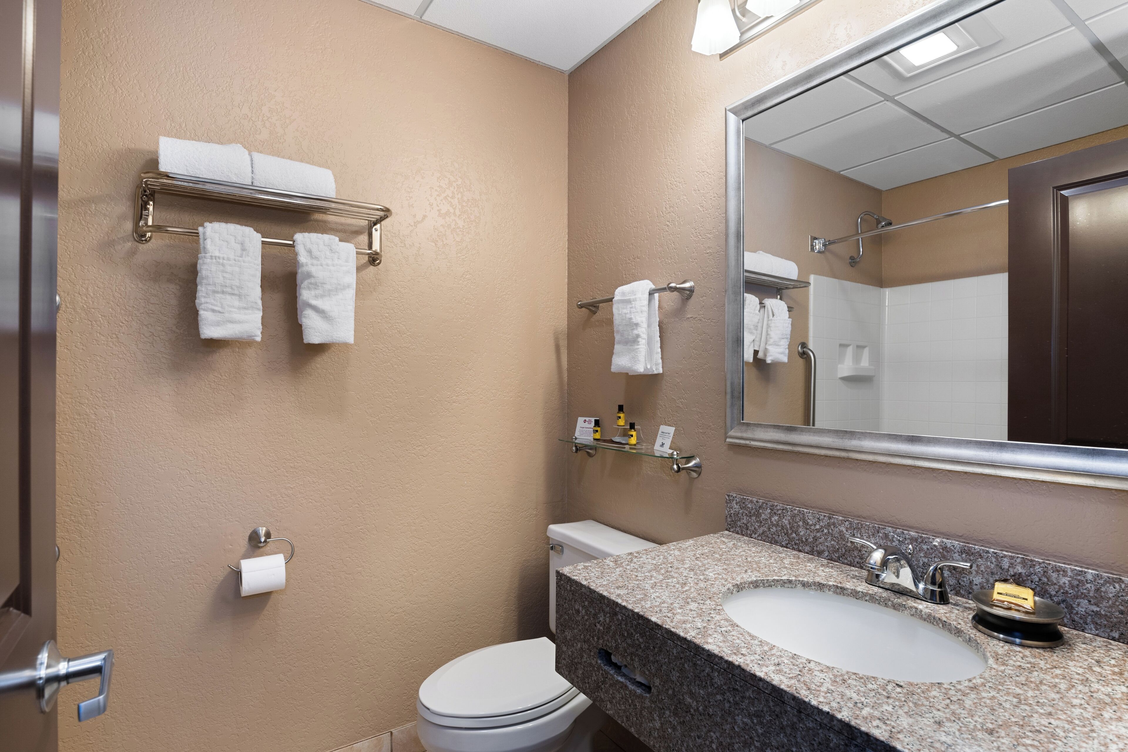 A bathroom with a beige wall, a white toilet, a granite sink, and a mirror.
