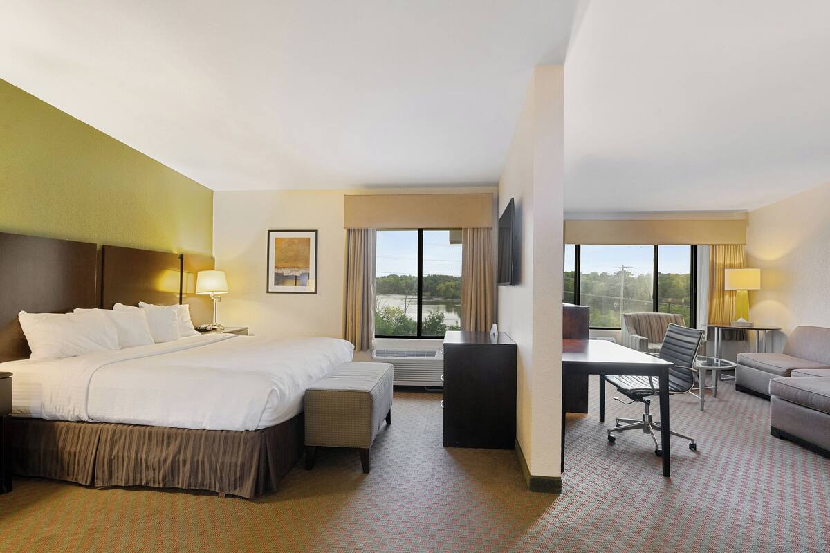 A hotel room with a large bed, a desk, a chair, a sofa, and a view of the outdoors.