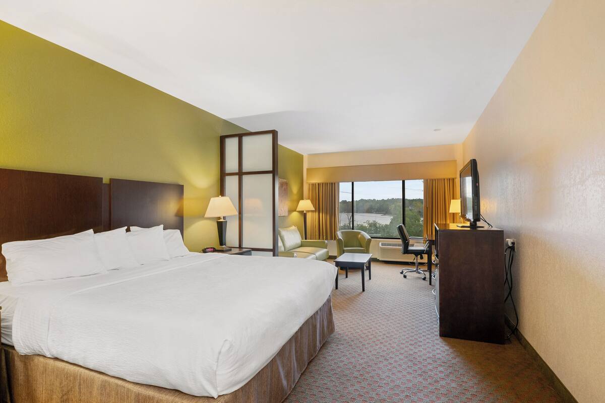 A hotel room with a large bed, a desk, a chair, a sofa, and a TV.