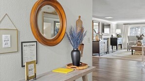 A reception area with a wooden bench, a welcome sign, a mirror, and a vase with blue decorative branches. - 3 King Suites · Hot Tub · Fireplace, 10 minutes to Walla Walla (College Place)