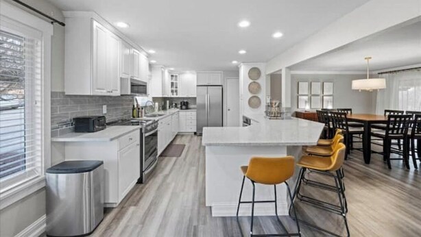 A modern kitchen with white cabinets, a central island, and a dining area with wooden chairs and a table. - 3 King Suites · Hot Tub · Fireplace, 10 minutes to Walla Walla (College Place)