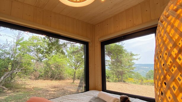 A room with wooden walls and ceiling, large windows, and a bed with patterned bedding. - La Bastide Provençale - Terre D'ocre & de Lavande (Viens)